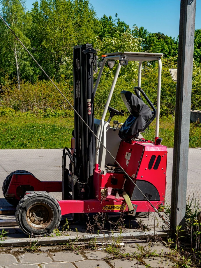 A red forklift parked outdoors on pavement.